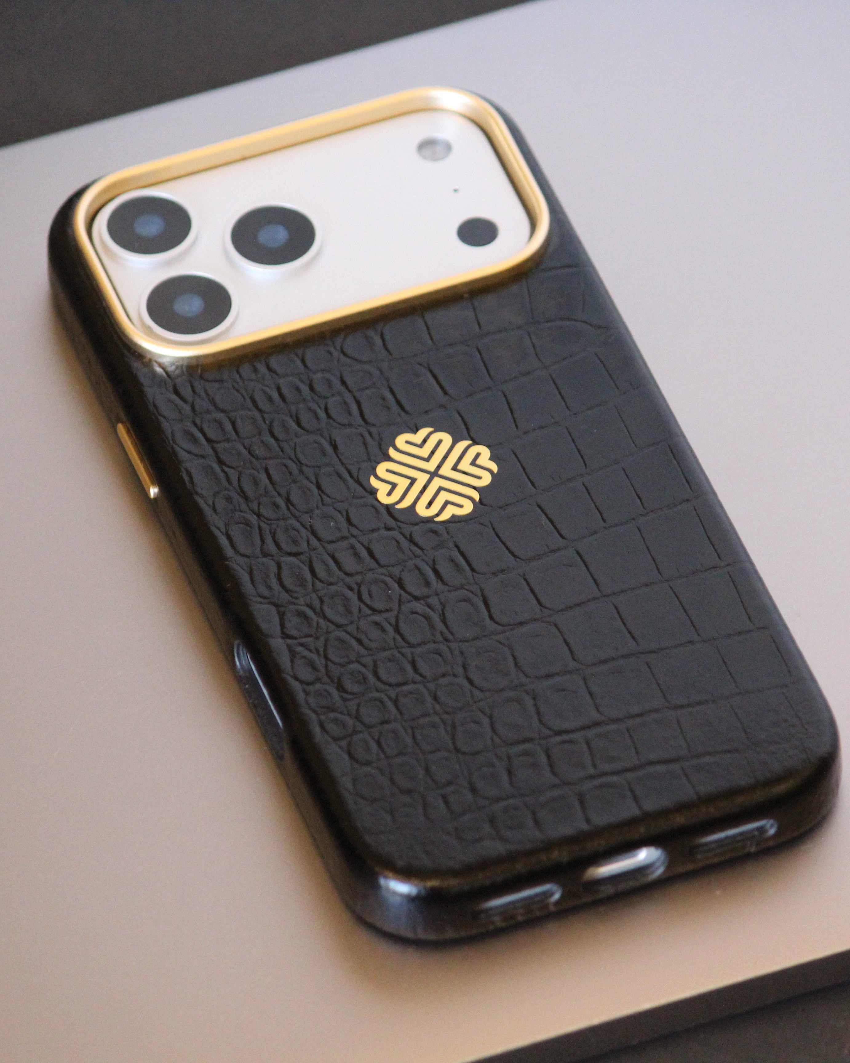 Black textured leather phone case with gold accents on a light gray surface