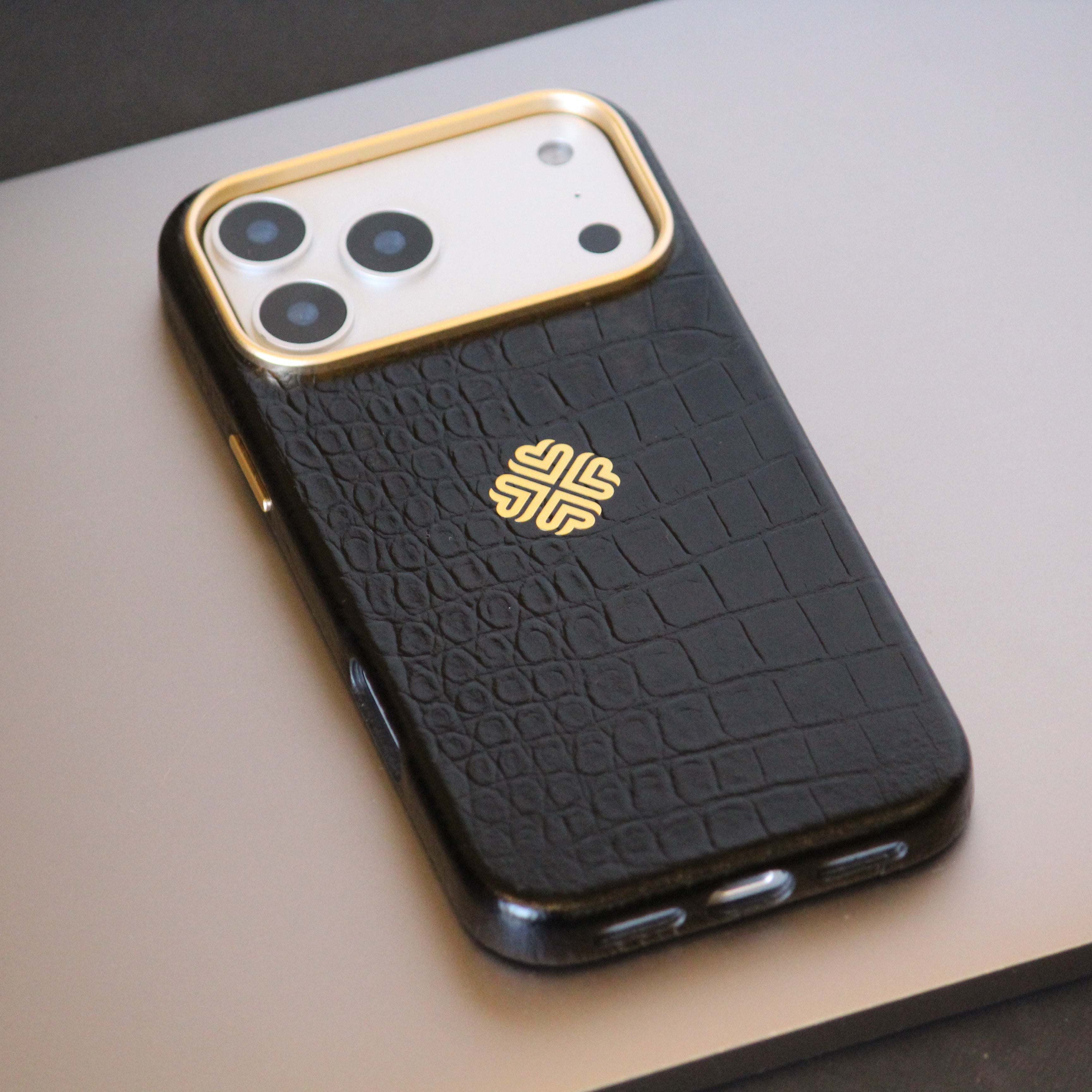 Black textured leather phone case with gold accents on a light gray surface